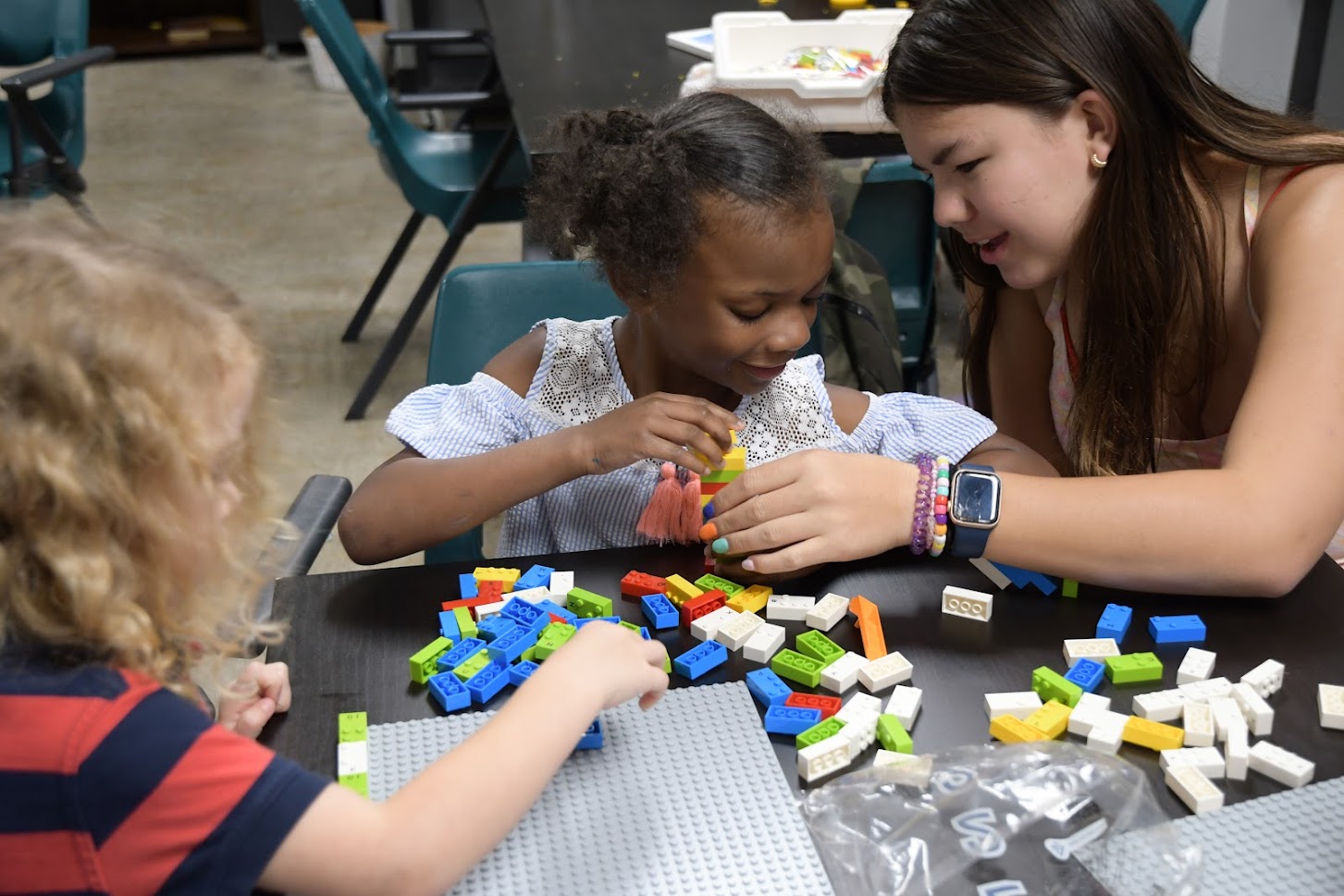 A volunteer is helping two children build Legos.