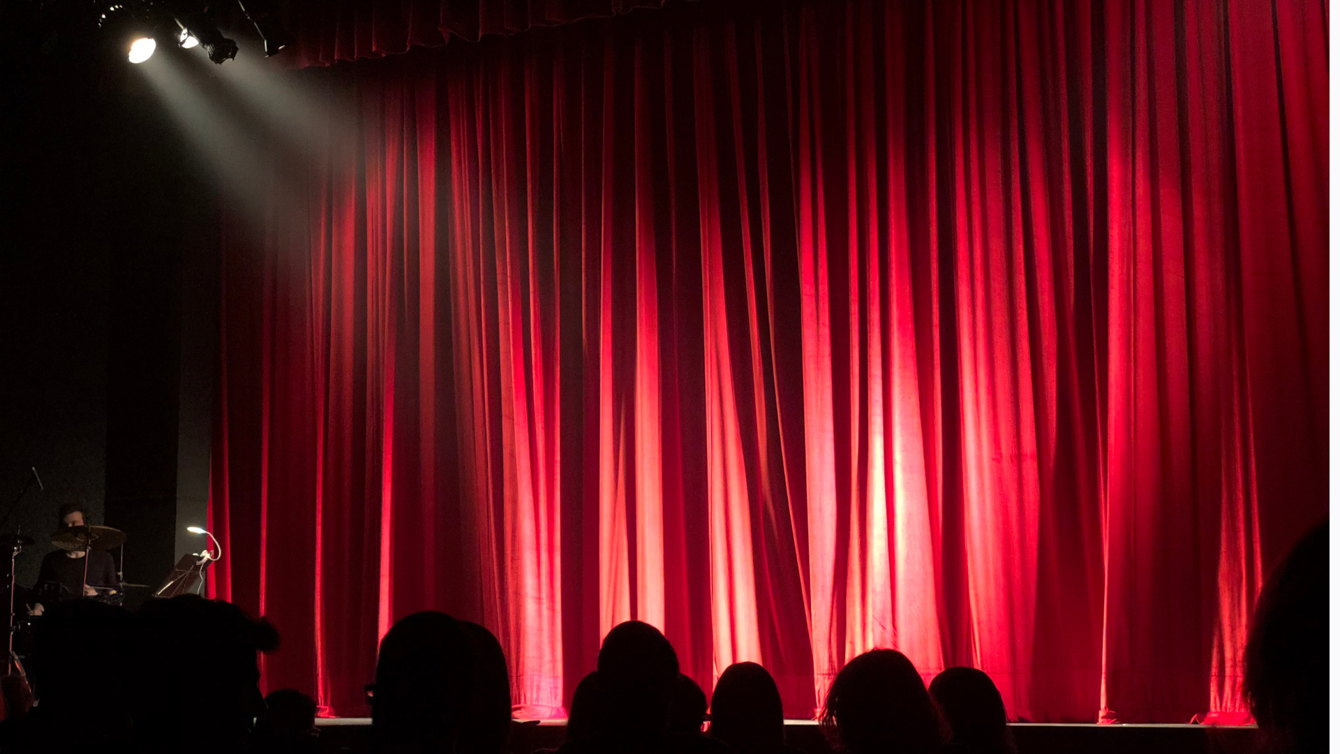A theater stage with a red curtain with bright lights shining on it.