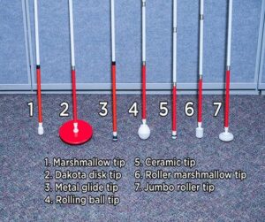 A picture of different white cane tips is shown from left to right.   
1) Marshmallow tip is shaped like a marshmallow
2) Dakota disk tip is a flat, small plate-sized tip
3) Metal glide tip is a round tip with a flat edge 
4) Rolling ball tip is a rounded ball that moves from left to right only. 
5) Ceramic tip is a round half-dome with a rubber band around. 
6) Roller marshmallow tip is shaped like a marshmallow but rolls left to right 
7) Jumbo roller tip is a flat wheel that moves left to right