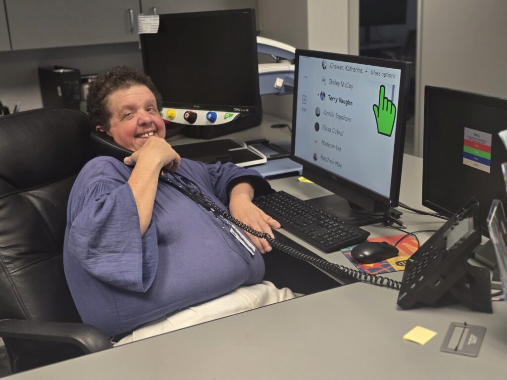 Photo of Thomas Morrison smiling while on the phone seated in front of a computer monitor at a desk.