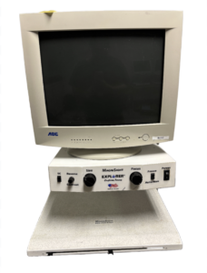 A MagniSight Explorer desktop video magnifier with an AOC monitor and control panel featuring knobs for size, focus, contrast, and reverse, along with buttons for freeze and auto/manual.