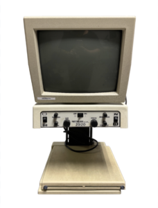 A close-up of a vintage Optilec 20/20 vision testing device with a CRT monitor and control panel.