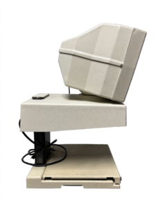 A beige computer monitor tilted back, resting on a beige base with a black power cord coiled underneath.