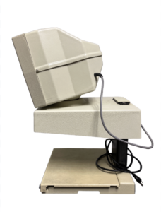 A beige computer monitor tilted back, resting on a beige base with a black power cord coiled underneath.
